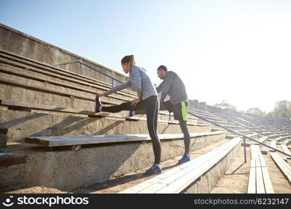 fitness, sport, exercising and lifestyle concept - couple stretching leg on stands of stadium