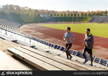 fitness, sport, exercising and lifestyle concept - happy couple running upstairs on stadium