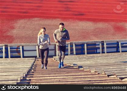 fitness, sport, exercising and lifestyle concept - happy couple running upstairs on stadium. happy couple running upstairs on stadium