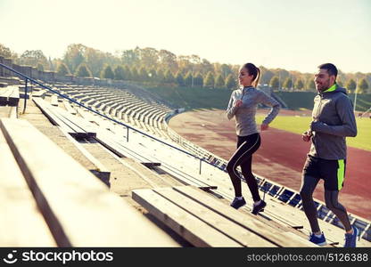 fitness, sport, exercising and lifestyle concept - happy couple running upstairs on stadium. happy couple running upstairs on stadium