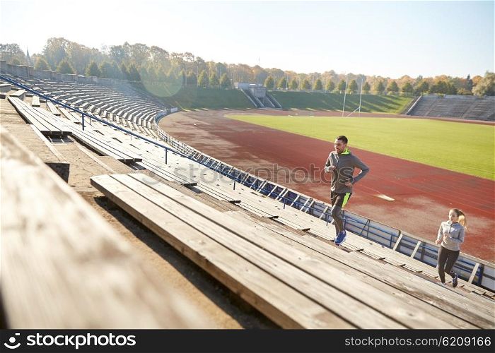 fitness, sport, exercising and lifestyle concept - happy couple running upstairs on stadium