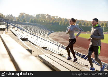 fitness, sport, exercising and lifestyle concept - happy couple running upstairs on stadium