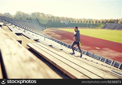 fitness, sport, exercising and people concept - happy young man running upstairs on stadium. happy young man running upstairs on stadium