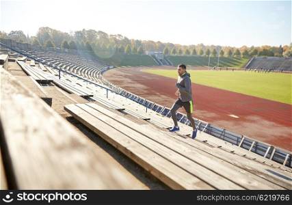 fitness, sport, exercising and people concept - happy young man running upstairs on stadium