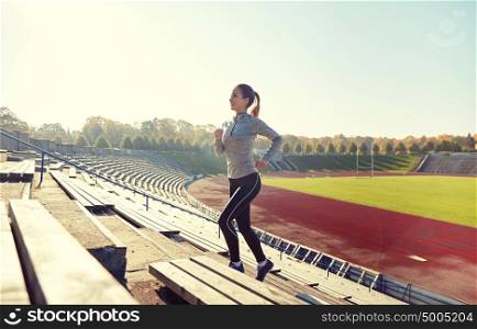 fitness, sport, exercising and people concept - happy young woman running upstairs on stadium. happy young woman running upstairs on stadium