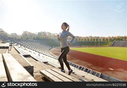 fitness, sport, exercising and people concept - happy young woman running upstairs on stadium