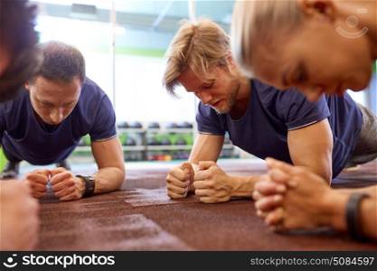 fitness, sport, exercising and people concept - man with heart-rate tracker at group training doing plank exercise in gym. group of people doing plank exercise in gym. group of people doing plank exercise in gym