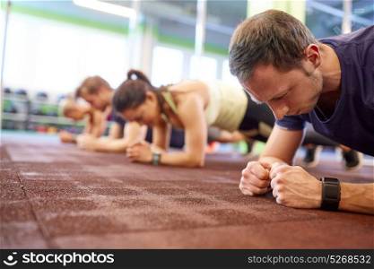 fitness, sport, exercising and people concept - man with heart-rate tracker at group training doing plank exercise in gym. man at group training doing plank exercise in gym