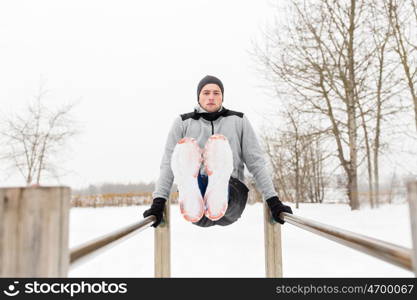 fitness, sport, exercising and people concept - young man doing abdominal exercise on parallel bars in winter