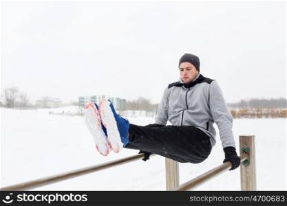 fitness, sport, exercising and people concept - young man doing abdominal exercise on parallel bars in winter