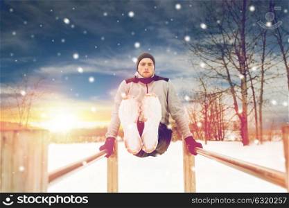 fitness, sport, exercising and people concept - young man doing abdominal exercise on parallel bars in winter. young man exercising on parallel bars in winter