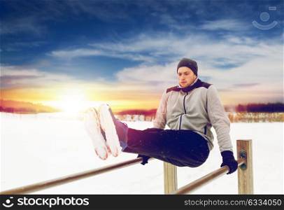 fitness, sport, exercising and people concept - young man doing abdominal exercise on parallel bars in winter. young man exercising on parallel bars in winter
