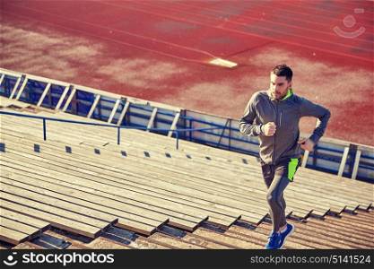 fitness, sport, exercising and people concept - young man running upstairs on stadium. young man running upstairs on stadium