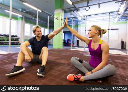 fitness, sport, exercising, gesture and people concept - happy couple resting and making high five in gym. happy couple making high five in gym