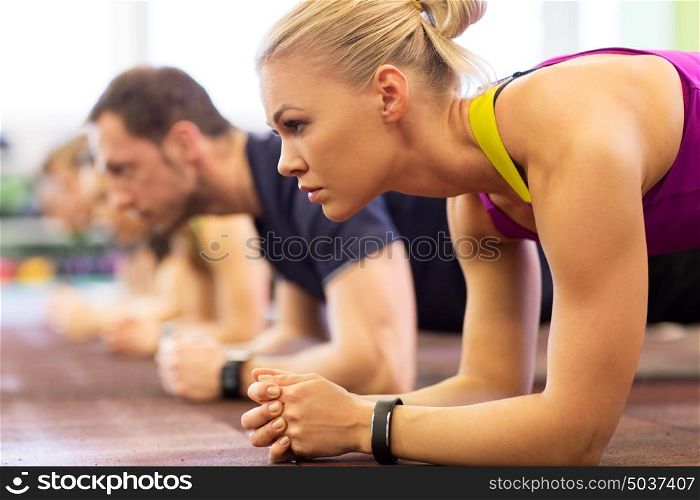fitness, sport, exercising, people and healthy lifestyle concept - close up of woman with heart-rate tracker at group training doing plank exercise in gym. close up of woman at training doing plank in gym