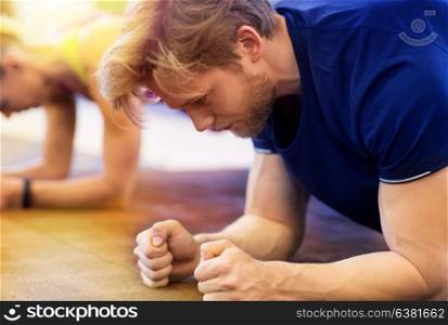 fitness, sport, exercising, people and healthy lifestyle concept - close up of man at group training doing plank exercise in gym. close up of man at training doing plank in gym