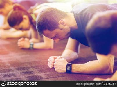 fitness, sport, exercising, people and healthy lifestyle concept - man with heart-rate tracker at group training doing plank exercise in gym. man with heart-rate tracker exercising in gym