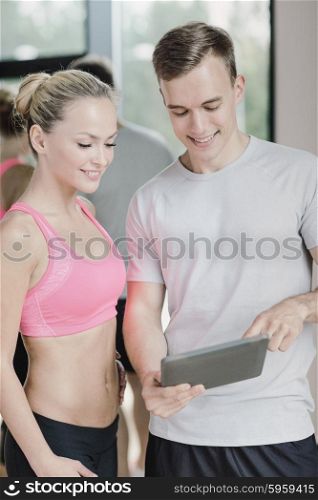fitness, sport, exercising, technology and diet concept - smiling young woman and personal trainer with tablet pc computer in gym
