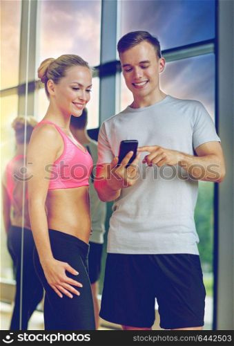 fitness, sport, exercising, technology and diet concept - smiling young woman and personal trainer with smartphone in gym. smiling young woman with personal trainer in gym