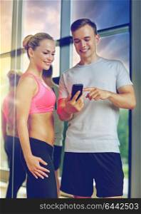 fitness, sport, exercising, technology and diet concept - smiling young woman and personal trainer with smartphone in gym. smiling young woman with personal trainer in gym