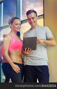 fitness, sport, exercising, technology and diet concept - smiling young woman and personal trainer with tablet pc computer in gym. smiling young woman with personal trainer in gym