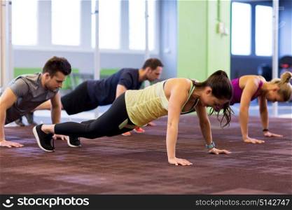 fitness, sport, exercising, training and healthy lifestyle concept - group of people doing straight arm plank in gym. group of people exercising in gym