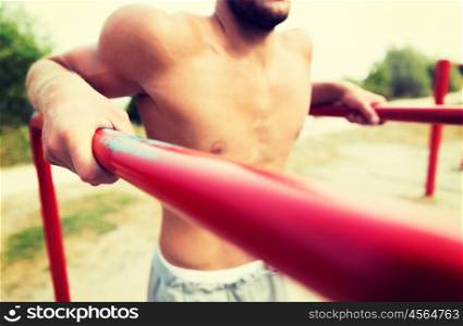 fitness, sport, exercising, training and lifestyle concept - close up of young man doing triceps dip on parallel bars outdoors