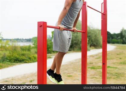 fitness, sport, exercising, training and lifestyle concept - close up of young man doing pull ups on horizontal bar outdoors