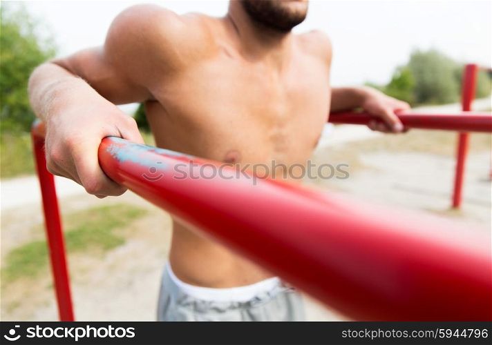 fitness, sport, exercising, training and lifestyle concept - close up of young man doing triceps dip on parallel bars outdoors