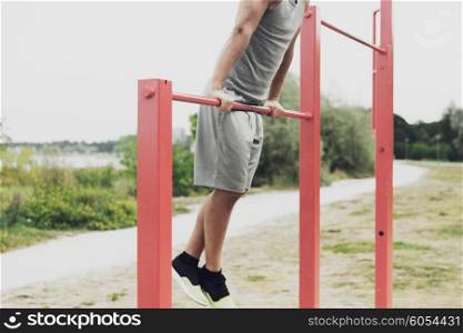 fitness, sport, exercising, training and lifestyle concept - close up of young man doing pull ups on horizontal bar outdoors