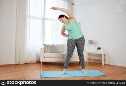 fitness, sport, exercising, training and lifestyle concept - smiling plus size woman stretching on mat at home
