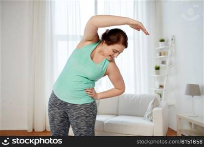 fitness, sport, exercising, training and lifestyle concept - smiling plus size woman stretching at home
