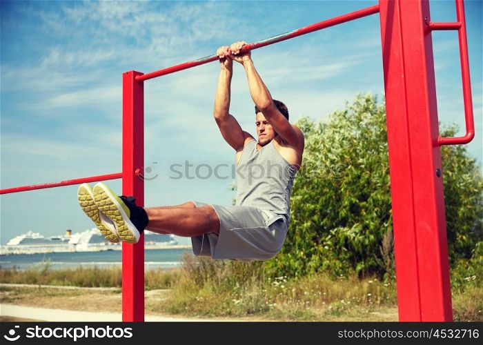fitness, sport, exercising, training and lifestyle concept - young man doing abdominal exercise on horizontal bar in summer park