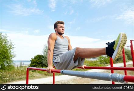 fitness, sport, exercising, training and lifestyle concept - young man doing abdominal exercise on parallel bars in summer park
