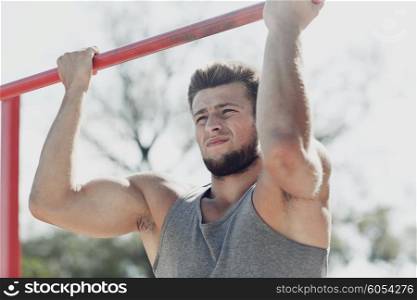 fitness, sport, exercising, training and lifestyle concept - young man doing pull ups on horizontal bar outdoors