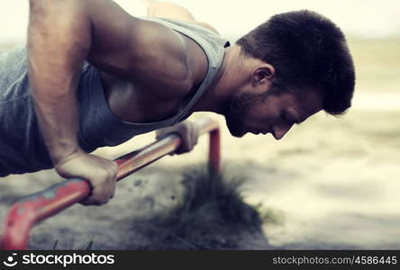 fitness, sport, exercising, training and lifestyle concept - young man doing push ups on horizontal bar outdoors