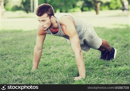 fitness, sport, exercising, training and lifestyle concept - young man doing push ups or plank exercise on grass in summer park