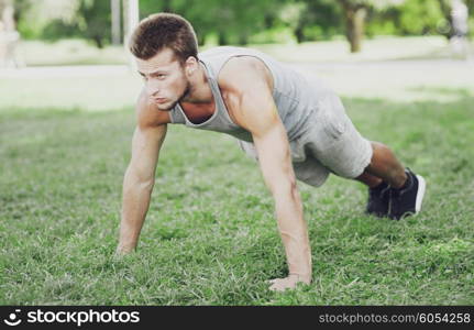 fitness, sport, exercising, training and lifestyle concept - young man doing push ups or plank exercise on grass in summer park