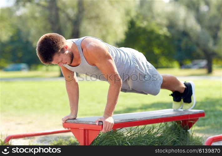 fitness, sport, exercising, training and lifestyle concept - young man doing push ups on bench at summer park