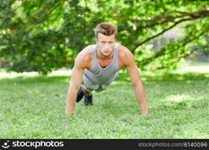 fitness, sport, exercising, training and lifestyle concept - young man doing push ups or plank exercise on grass in summer park