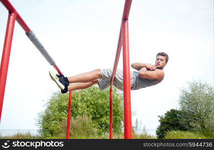 fitness, sport, exercising, training and lifestyle concept - young man doing sit up on parallel bars in summer park