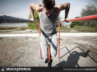 fitness, sport, exercising, training and lifestyle concept - young man doing triceps dip with weight belt on parallel bars outdoors