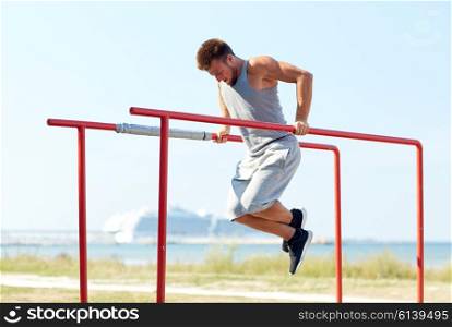 fitness, sport, exercising, training and lifestyle concept - young man doing triceps dip on parallel bars outdoors