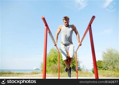 fitness, sport, exercising, training and lifestyle concept - young man doing triceps dip with weight belt on parallel bars outdoors