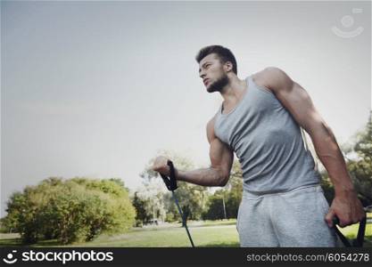 fitness, sport, exercising, training and lifestyle concept - young man exercising with expander in summer park