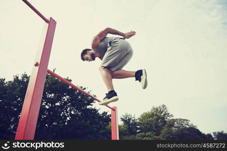 fitness, sport, exercising, training and lifestyle concept - young man jumping on horizontal bar outdoors