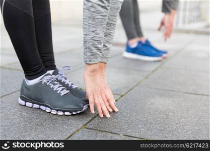 fitness, sport, exercising, training and people concept - close up of couple stretching on city street