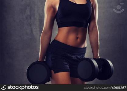 fitness, sport, exercising, training and people concept - close up of young woman flexing muscles with dumbbells in gym. young woman flexing muscles with dumbbells in gym