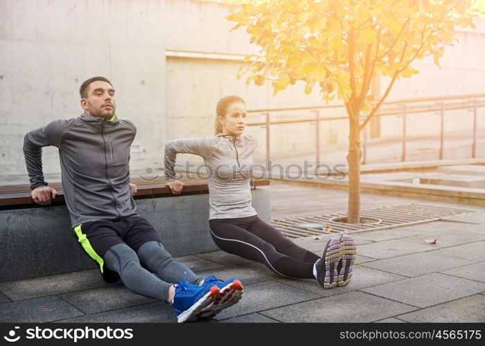 fitness, sport, exercising, training and people concept - couple doing triceps dip exercise on city street bench