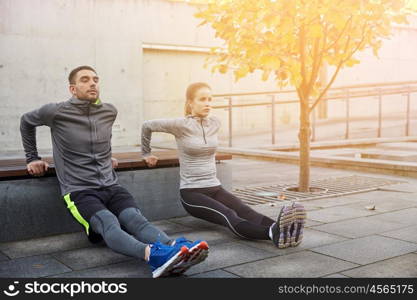 fitness, sport, exercising, training and people concept - couple doing triceps dip exercise on city street bench